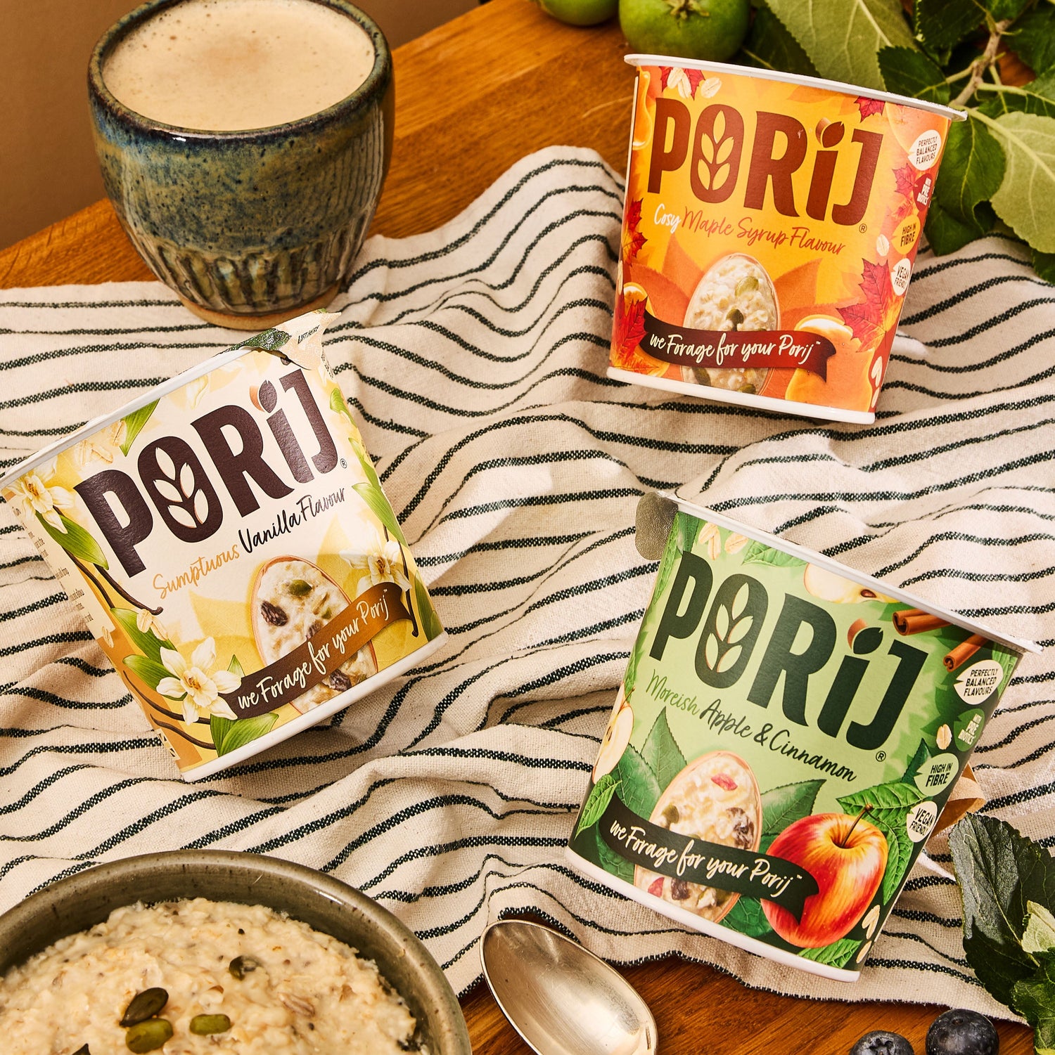 Porij porridge pots packaging on a table with a bowl of food and a cup of coffee.