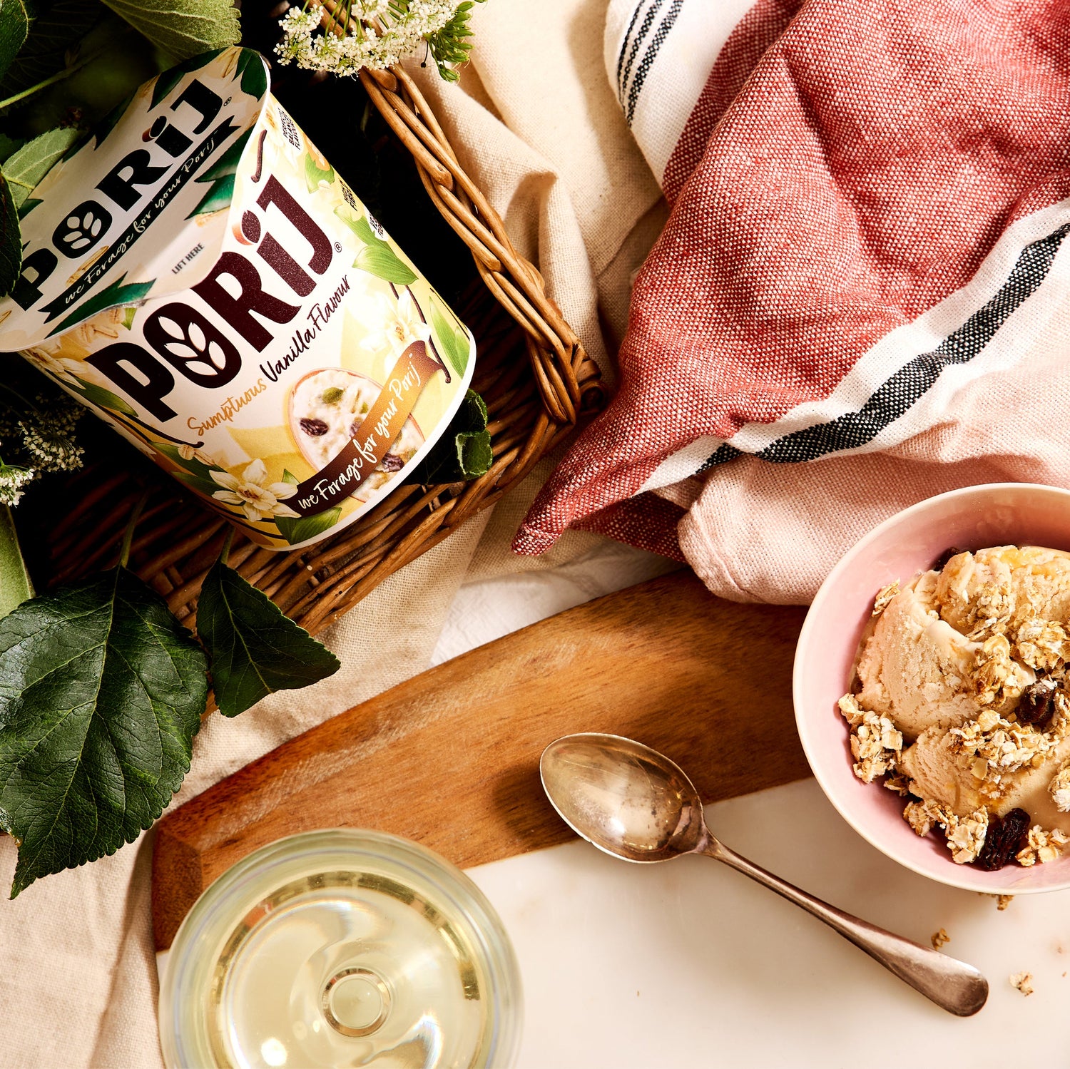Bowl of ice cream with a spoon, a pot of porridge, and a pink towel on a wooden board.